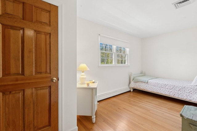 bedroom featuring a baseboard heating unit, baseboards, visible vents, and light wood-type flooring