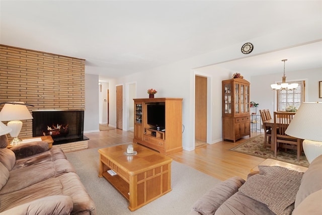 living area featuring a brick fireplace, a chandelier, light wood-style floors, and baseboards