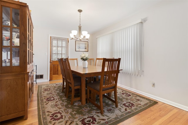 dining space featuring visible vents, light wood-style flooring, an inviting chandelier, and baseboards