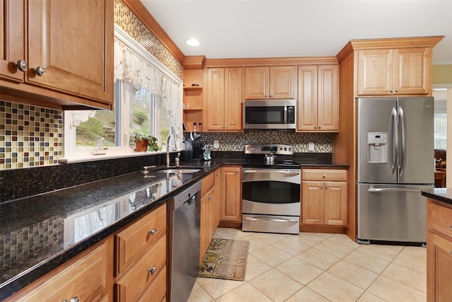 kitchen with dark stone counters, tasteful backsplash, light tile patterned flooring, a sink, and stainless steel appliances