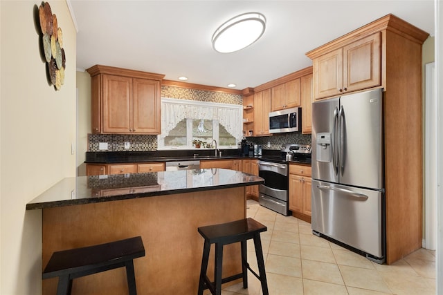 kitchen with tasteful backsplash, light tile patterned floors, a sink, appliances with stainless steel finishes, and a kitchen breakfast bar