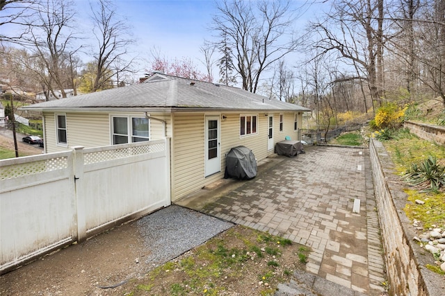 rear view of house featuring a patio, fence, and a shingled roof