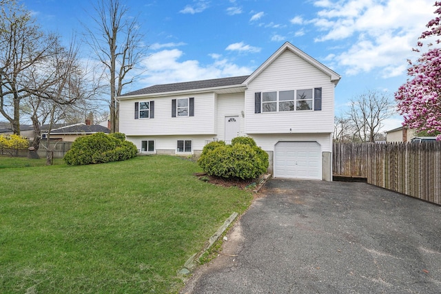 raised ranch with an attached garage, driveway, a front yard, and fence