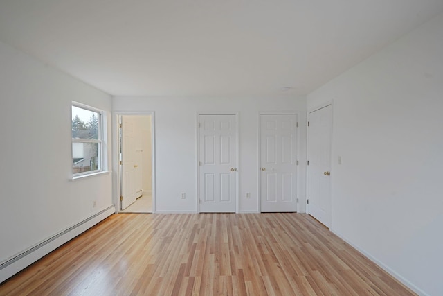 unfurnished bedroom with light wood finished floors, ensuite bathroom, a baseboard radiator, and baseboards