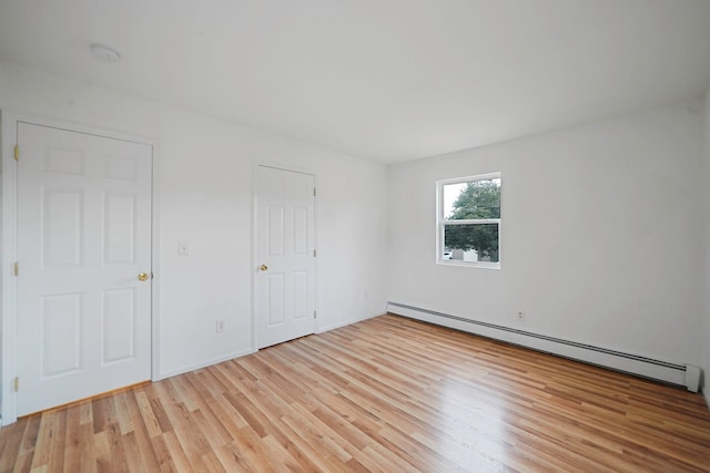 unfurnished bedroom with light wood-style flooring, a baseboard radiator, and baseboards