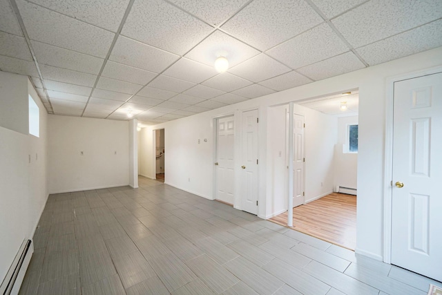 interior space featuring baseboard heating, a drop ceiling, and baseboards