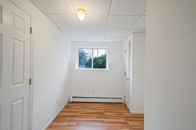 unfurnished room featuring light wood-style flooring, a drop ceiling, a baseboard heating unit, and baseboards
