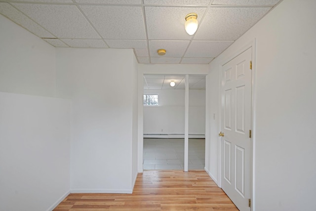 hall featuring a baseboard radiator, a paneled ceiling, baseboards, and light wood-type flooring