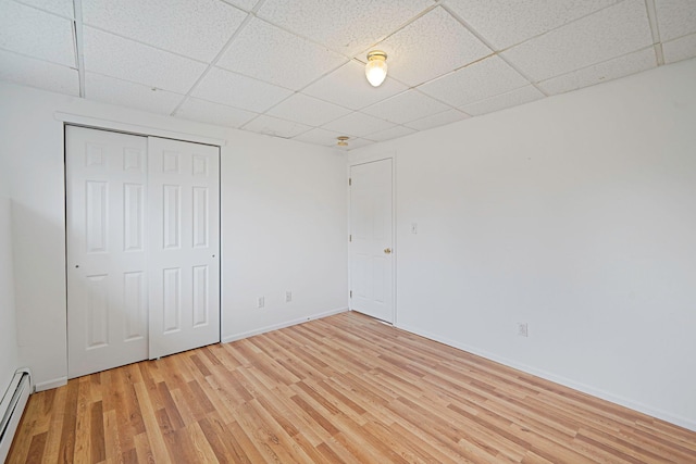 unfurnished bedroom featuring a paneled ceiling, a closet, baseboards, and light wood-style floors