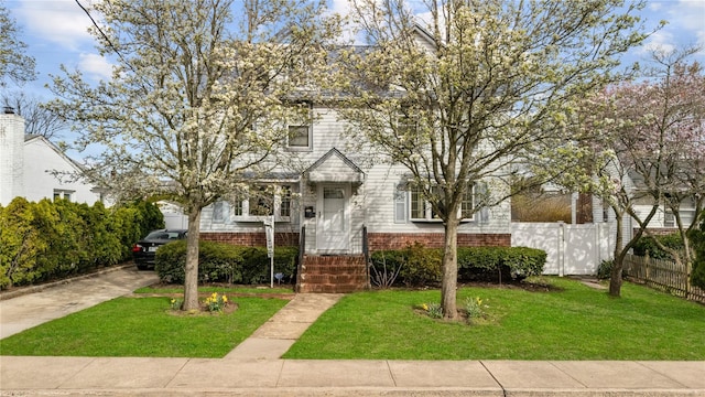 view of front of home with brick siding, fence, driveway, and a front yard