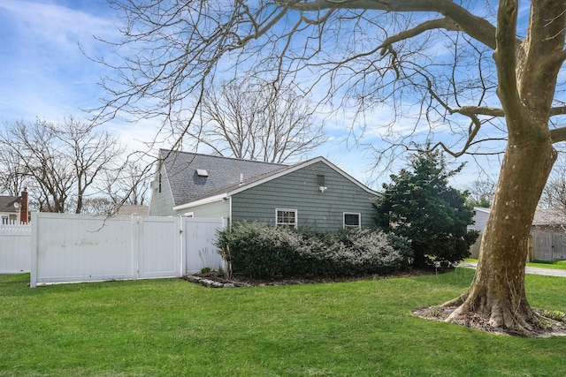 view of side of home featuring fence, roof with shingles, a gate, and a lawn