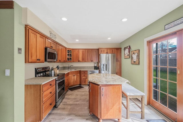 kitchen featuring recessed lighting, brown cabinetry, appliances with stainless steel finishes, a kitchen island, and light wood-type flooring