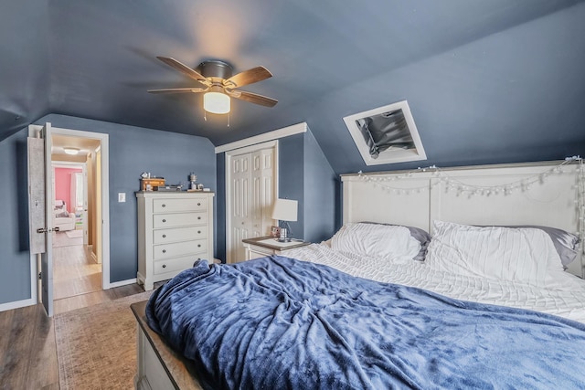 bedroom featuring ceiling fan, baseboards, wood finished floors, vaulted ceiling, and a closet