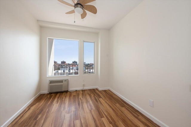 unfurnished room with a wall unit AC, wood finished floors, baseboards, and a ceiling fan
