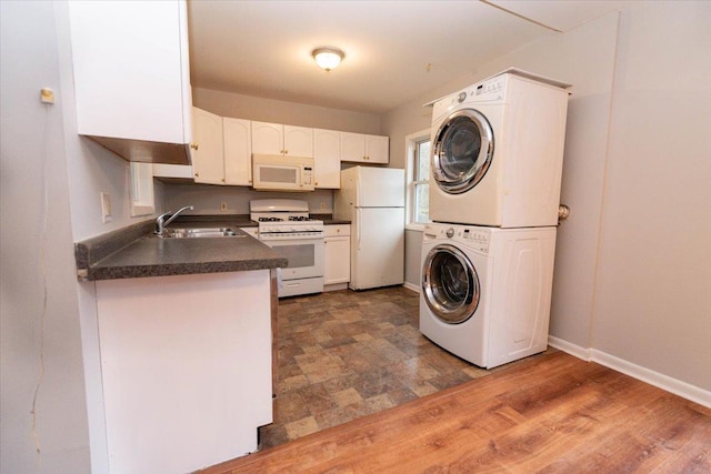 700 Sackett Lake Rd, Monticello, NY 12701 - kitchen featuring white cabinets, a sink, dark countertops, white appliances, and stacked washer and dryer