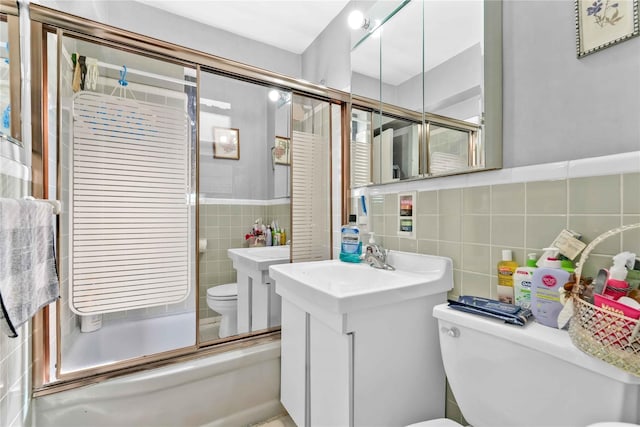 bathroom with combined bath / shower with glass door, vanity, tile walls, a wainscoted wall, and toilet