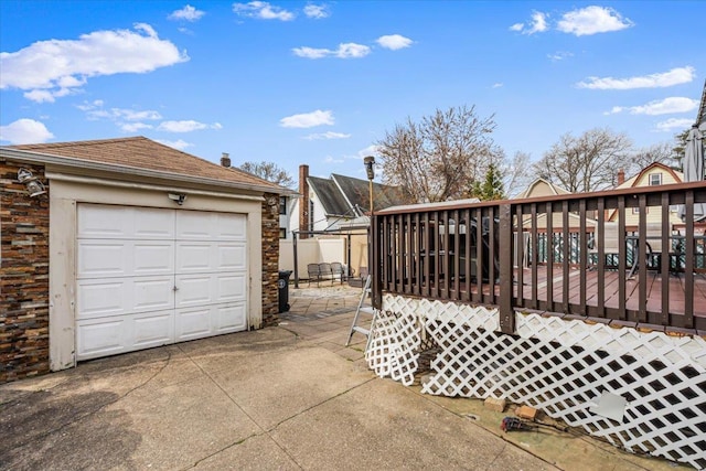 exterior space featuring an outbuilding, a garage, roof with shingles, concrete driveway, and a deck