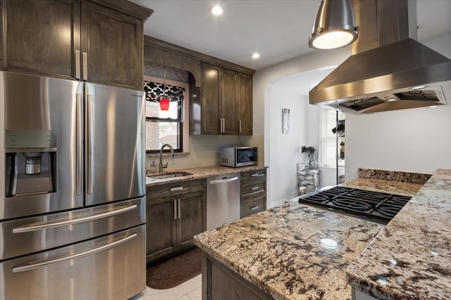 kitchen with a sink, appliances with stainless steel finishes, dark brown cabinetry, light stone countertops, and island range hood