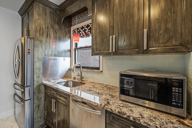kitchen featuring appliances with stainless steel finishes, light stone counters, dark brown cabinets, decorative backsplash, and a sink