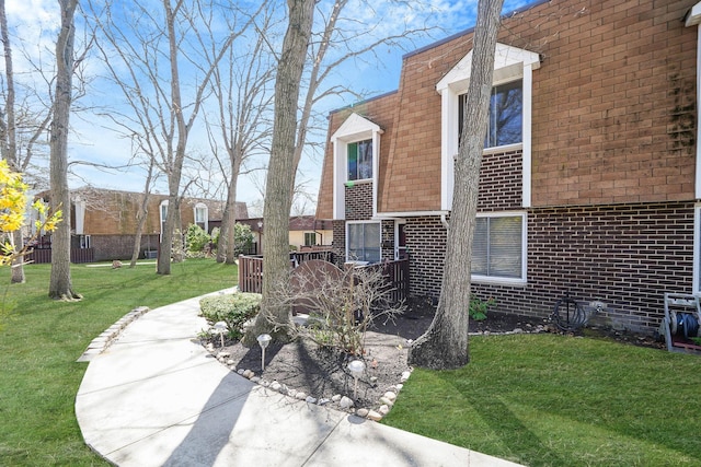 view of property exterior featuring brick siding, mansard roof, and a yard