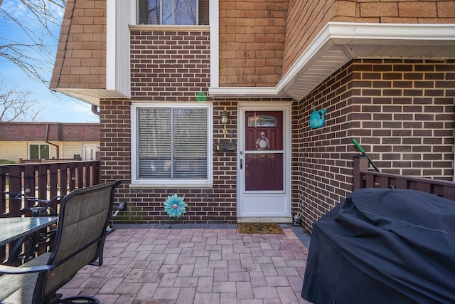 view of exterior entry with a patio and brick siding