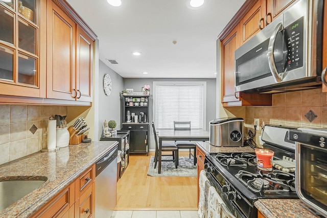 kitchen featuring brown cabinets, stainless steel appliances, stone countertops, and glass insert cabinets