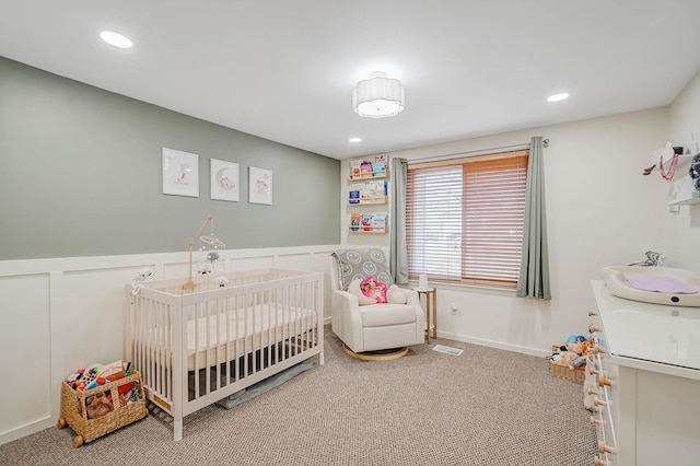 carpeted bedroom with visible vents, a wainscoted wall, a nursery area, and recessed lighting