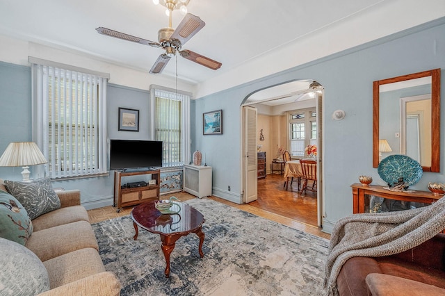 living area with arched walkways, wood finished floors, baseboards, and ceiling fan