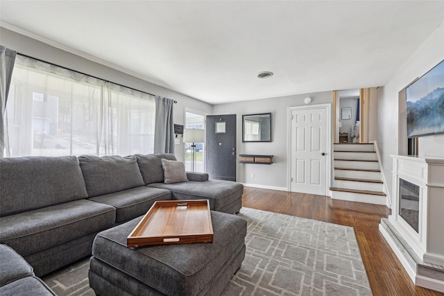 living area with visible vents, baseboards, dark wood-style flooring, and stairs