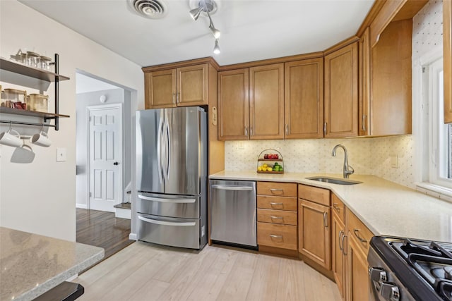 kitchen featuring appliances with stainless steel finishes, a sink, light wood finished floors, brown cabinetry, and visible vents