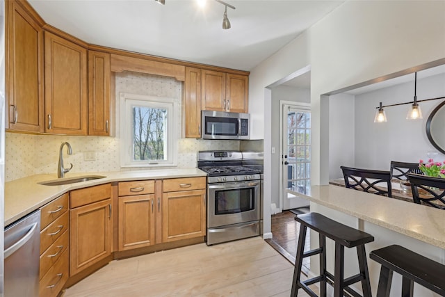 kitchen with brown cabinets, stainless steel appliances, a sink, and light wood finished floors