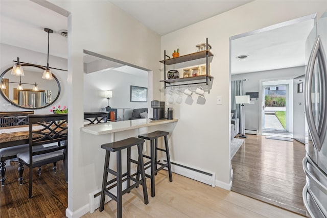 kitchen featuring baseboard heating, light countertops, a kitchen breakfast bar, light wood-style flooring, and freestanding refrigerator