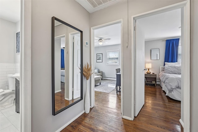 hallway featuring dark wood-style flooring, baseboards, visible vents, and a baseboard heating unit