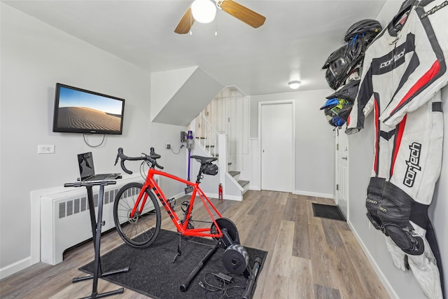 exercise area featuring baseboards, a ceiling fan, wood finished floors, and radiator heating unit