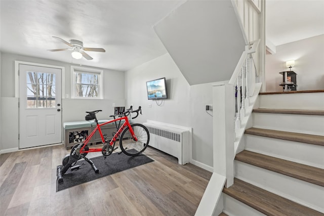 exercise room with wood finished floors, baseboards, ceiling fan, and radiator heating unit