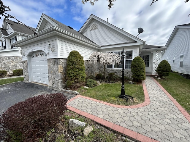 view of front of home featuring a garage, a front yard, stone siding, and aphalt driveway