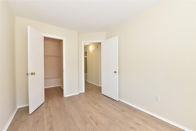 unfurnished bedroom with a walk in closet, baseboards, light wood-type flooring, and a closet