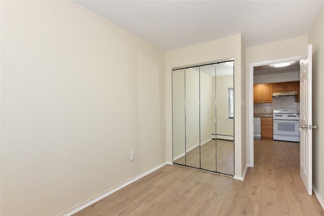 unfurnished bedroom featuring light wood-style flooring, a closet, baseboards, and baseboard heating