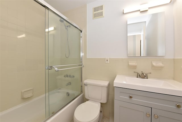 bathroom with tile walls, toilet, vanity, visible vents, and enclosed tub / shower combo