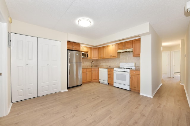 kitchen featuring a sink, light wood-type flooring, backsplash, light countertops, and appliances with stainless steel finishes