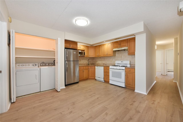 kitchen featuring independent washer and dryer, light wood-style flooring, a sink, decorative backsplash, and appliances with stainless steel finishes