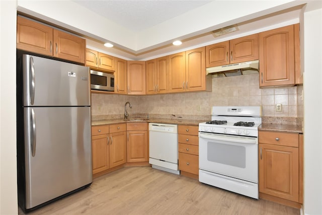 kitchen with light wood-style flooring, under cabinet range hood, a sink, stainless steel appliances, and tasteful backsplash