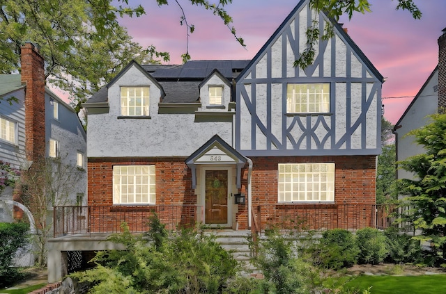 tudor house featuring roof mounted solar panels, stucco siding, a shingled roof, and brick siding