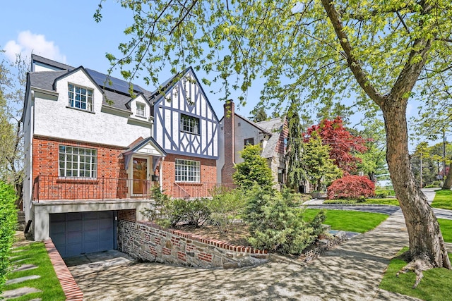 tudor home featuring brick siding, a garage, stucco siding, concrete driveway, and solar panels