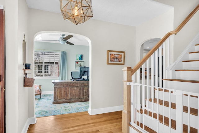 stairs with arched walkways, baseboards, and wood finished floors