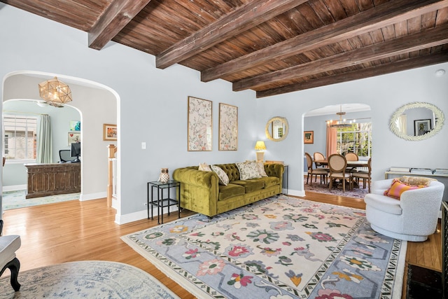 living room featuring an inviting chandelier, wood finished floors, beam ceiling, wooden ceiling, and arched walkways