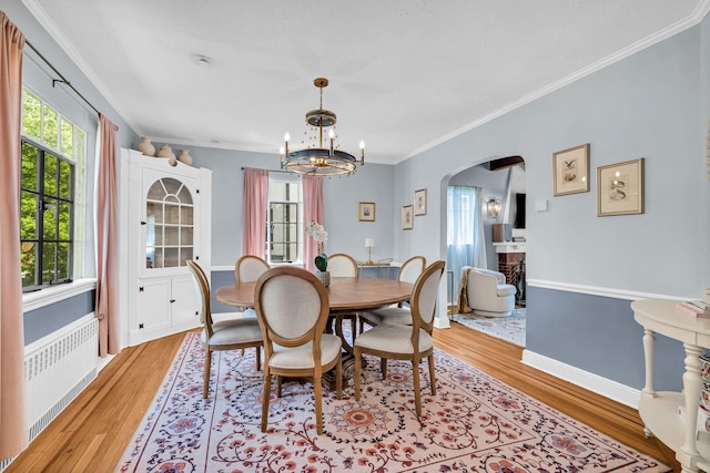 dining room with light wood finished floors, arched walkways, a chandelier, radiator, and ornamental molding