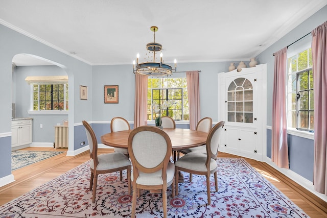 dining space with arched walkways, baseboards, a notable chandelier, and light wood-style flooring