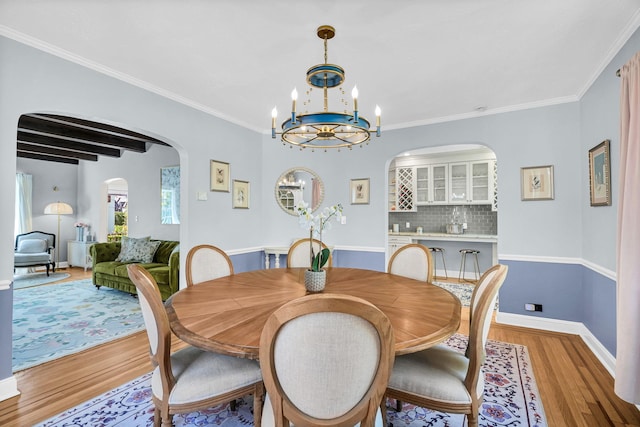 dining room featuring crown molding, arched walkways, baseboards, light wood finished floors, and a notable chandelier