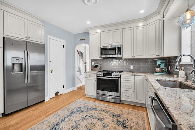 kitchen featuring arched walkways, appliances with stainless steel finishes, decorative backsplash, and a sink